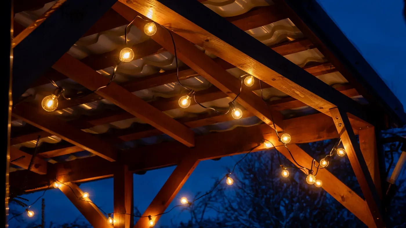 Uteplats i trädgården med pergola, trästaket och belysning i skymningen